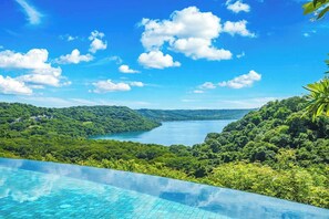 Une piscine à débordement offrant une vue imprenable sur une vallée verdoyante et un lac.