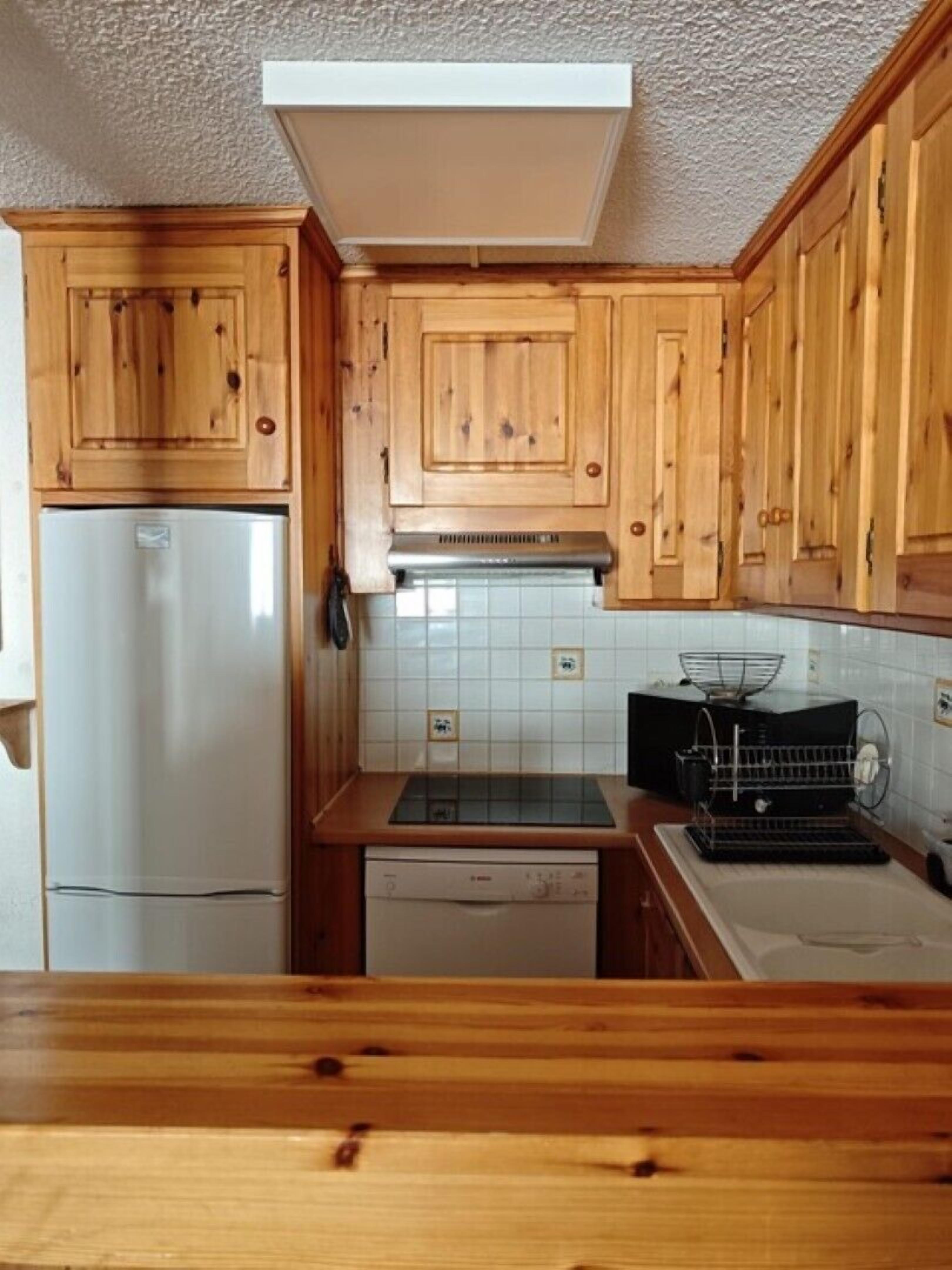 A kitchen with wooden cabinets, a stainless steel refrigerator, a dishwasher, and a tiled backsplash.