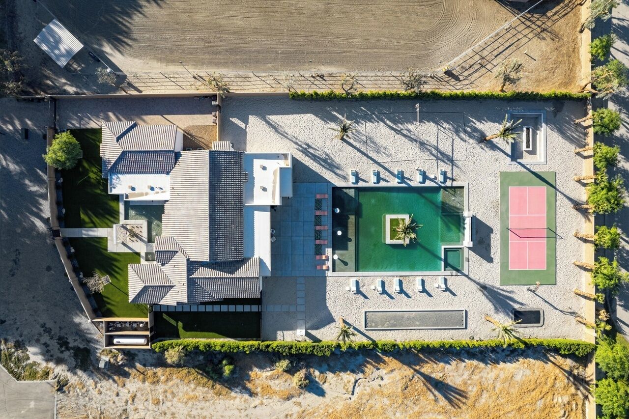 An aerial view of a modern building with a rooftop terrace, a swimming pool, and a tennis court.