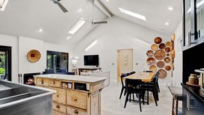 A modern kitchen with a central island, wooden cabinetry, and a dining area with a large table and chairs.