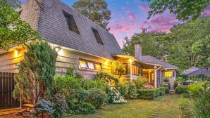 A two-story house with a sloped roof, a front porch, and a well-maintained garden.