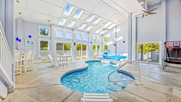 An indoor swimming pool with a sunroof, a basketball hoop, and a slide. - Soundfront Home w/ Indoor Pool, Hot Tub, Elevator, Game Room, Tiki Bar, Theater (Avon)