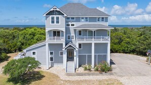 A two-story house with a balcony, a garage, and a view of the ocean. - Soundfront Home w/ Indoor Pool, Hot Tub, Elevator, Game Room, Tiki Bar, Theater (Avon)