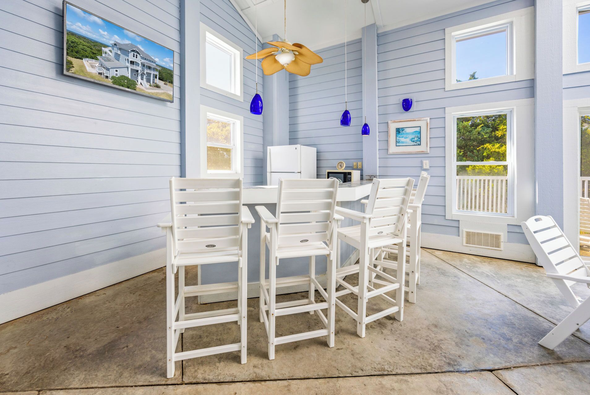 A dining area with a white table and chairs, a ceiling fan, and a kitchen area with a refrigerator and microwave.