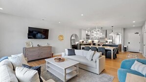 A modern living room with a sofa, coffee table, and TV. There is a kitchen area with a dining table and chairs. - Walloon Village 1 Bedroom Condo Across From The Lake! 7 night minimum. (Walloon Village)