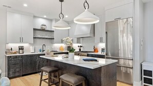 A modern kitchen with white cabinetry, a central island with stools, stainless steel appliances, and pendant lighting. - Walloon Village 1 Bedroom Condo Across From The Lake! 7 night minimum. (Walloon Village)