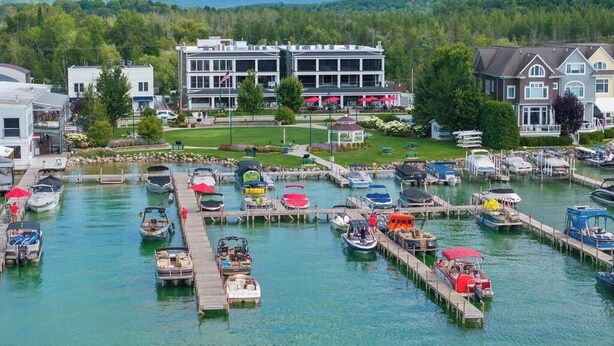 A marina with various boats docked, a building with a flag, and a grassy area with a gazebo. - Walloon Village 1 Bedroom Condo Across From The Lake! 7 night minimum. (Walloon Village)