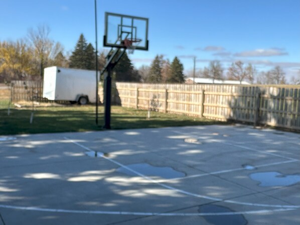 Ein Basketballplatz im Freien mit Korb, einem weißen Anhänger und einem Holzzaun.