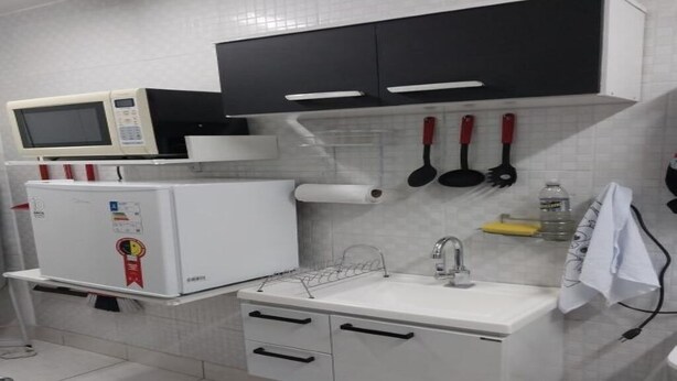 Una cocina compacta con microondas, refrigerador, lavabo y armarios negros.