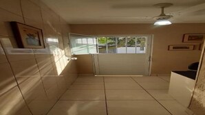 Un pasillo estrecho con paredes y suelo de baldosas, un ventilador de techo y una puerta con ventanal.