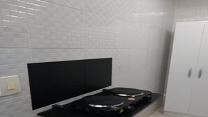 Cocina con dos cocinas de inducción negras sobre una encimera negra, salpicadero blanco con azulejos y un mueble blanco a la derecha.