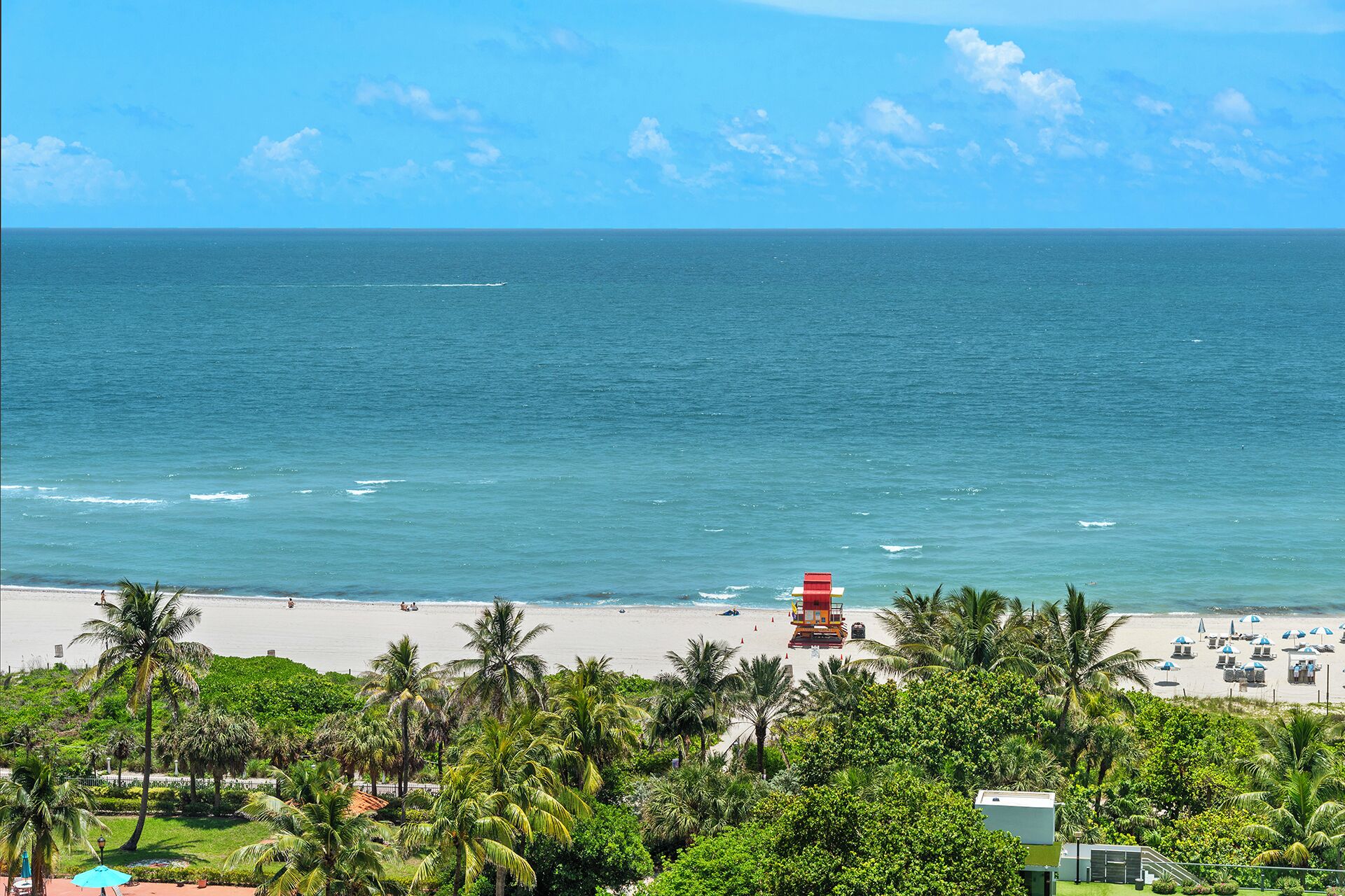 A beach with a lifeguard tower, palm trees, and beach umbrellas.