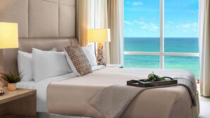 Ein Hotelzimmer mit einem großen Bett, zwei Nachttischlampen, einem Nachttisch mit Pflanze und Blick auf das Meer.