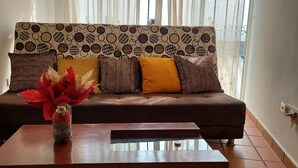 A living room with a brown sofa, patterned cushions, and a vase with red flowers on a wooden coffee table. - Enjoy the historical center of Cali  (Cali)