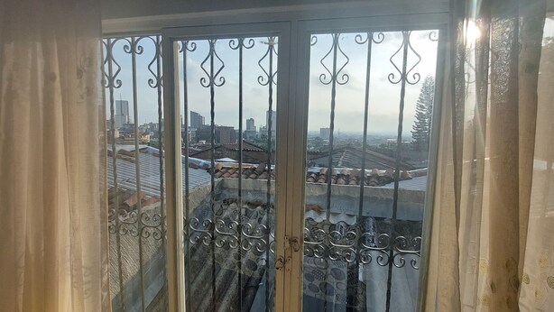 A view through a window with decorative iron bars and curtains, revealing a cityscape with buildings and rooftops. - Enjoy the historical center of Cali  (Cali)
