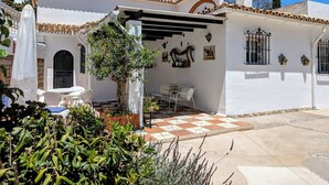 Eine weiße Villa mit einem Ziegeldach, einer überdachten Terrasse und einem Garten mit verschiedenen Pflanzen.