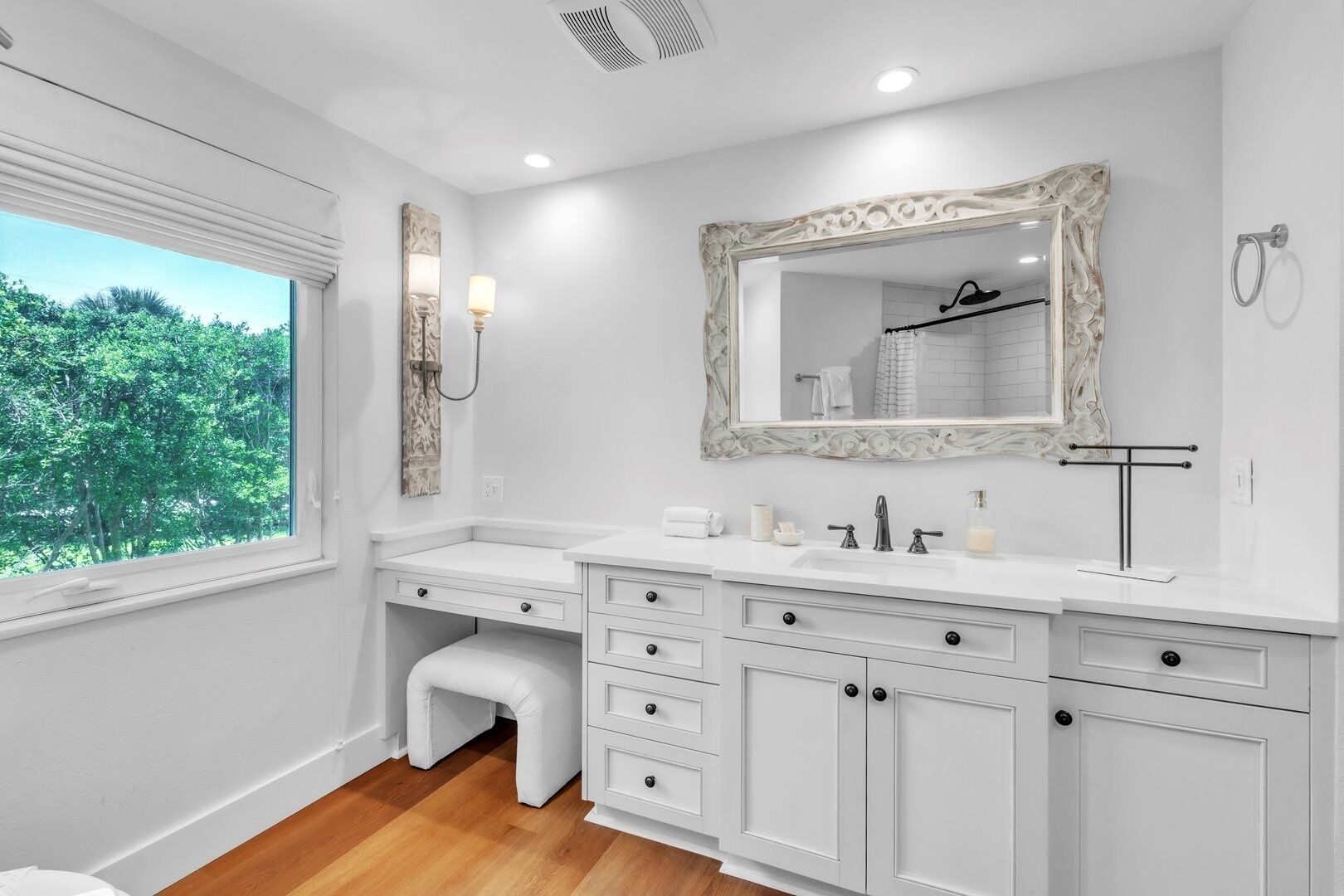A bathroom with a large window, a vanity with a mirror, and a shower area.