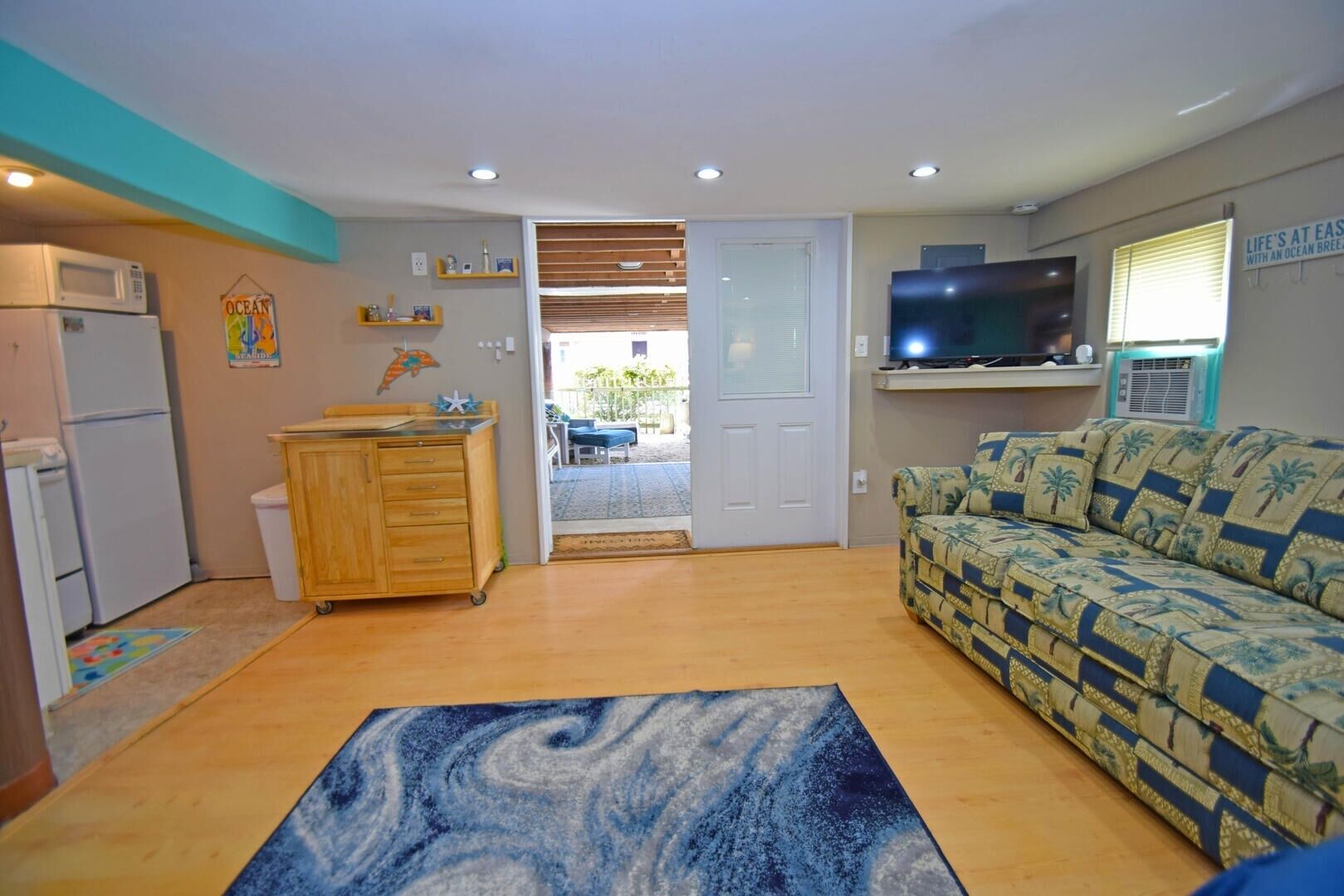 A compact living space with a kitchenette, a sofa, a TV, and a door leading to an outdoor area.