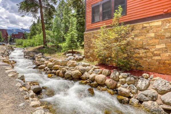 A stream flowing through a rocky bed, surrounded by trees and a building with a stone foundation.