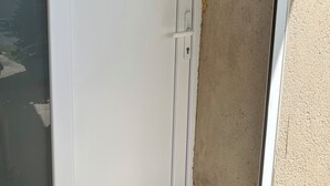Een witte deur met een schuifglasraam, een klein raam en twee stopcontacten in de muur.