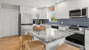 Une cuisine moderne avec des meubles blancs, un plan de travail en marbre et des appareils électroménagers en acier inoxydable.