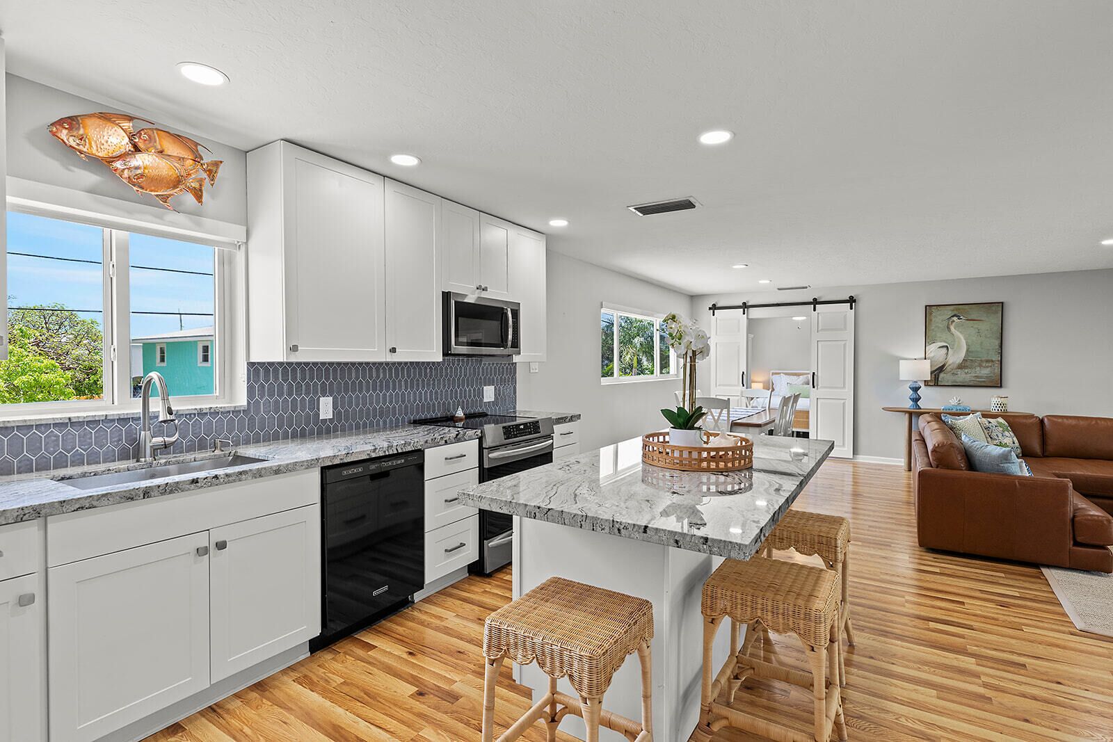 A modern kitchen with white cabinets, a large island with bar stools, a microwave, and a view of the outdoors.