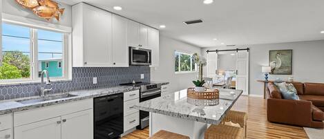 A modern kitchen with white cabinets, a large island with bar stools, a microwave, and a view of the outdoors.