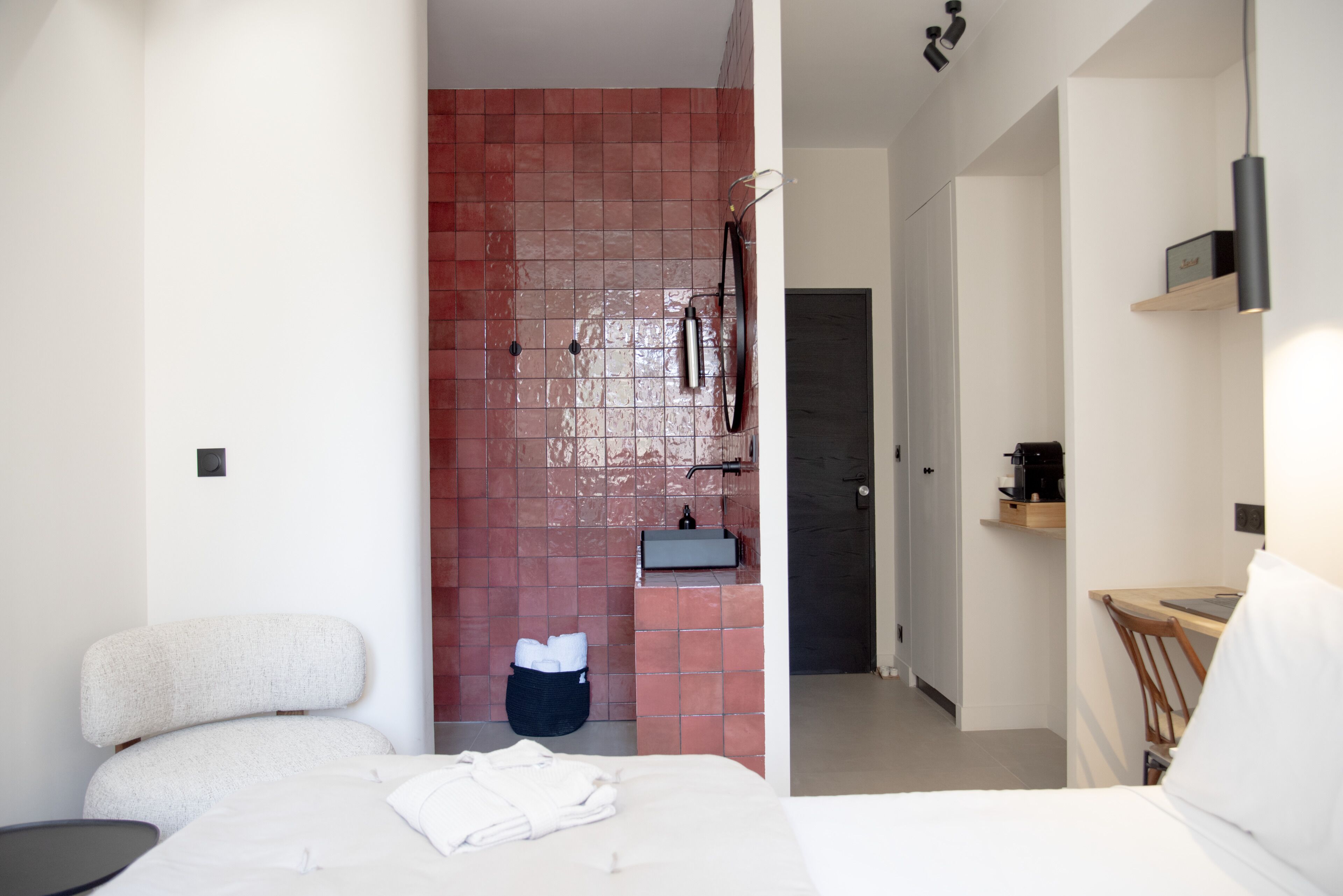 Quarto de hotel moderno com uma cama, uma pequena mesa, uma cadeira, pia e área de chuveiro.