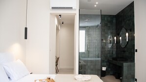 A modern hotel room with a bed, breakfast tray, and a bathroom with a glass shower and dark tiles. - Mouchki (Marseille)