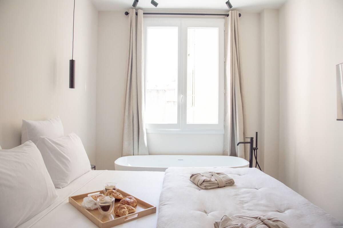 Ein Hotelzimmer mit einem Bett, einem kleinen Tisch, einem Fenster mit Vorhängen und einer Serviertschale mit Gebäck.