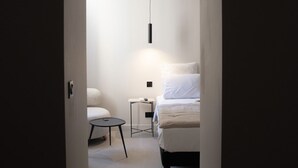 A narrow hallway leading to a bedroom with a bed, bedside table, and a hanging light fixture. - Mouchki (Marseille)