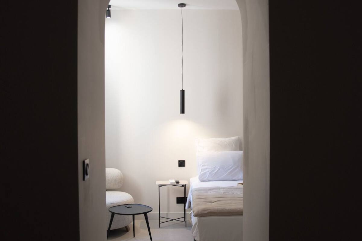 Ein schmaler Flur, der zu einem Schlafzimmer mit Bett, Nachttisch und Pendelleuchte führt.