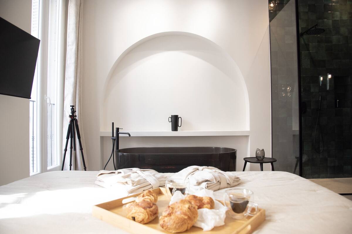 Ein Hotelzimmer mit einem Bett, einer Croissant-Platte, einer Kaffeetasse und einer Duschkabine.