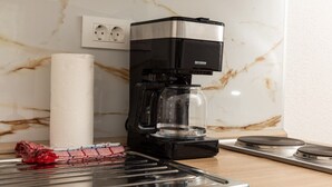 Une machine à café posée sur un plan de travail de cuisine, avec un pare-éclaboussures en marbre et une prise de courant au-dessus.