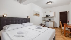 A hotel room with a large bed, a small kitchenette, a dining table, and a chair. - Studio Apartment 6 for two persons (Omisalj)