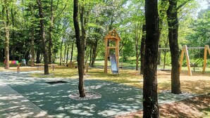 A park with a playground, including swings and a slide, surrounded by trees. - Studio Apartment 6 for two persons (Omisalj)