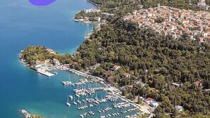 Vue aérienne d’une ville côtière avec un port de plaisance, des collines densément boisées et une mer bleue et limpide.