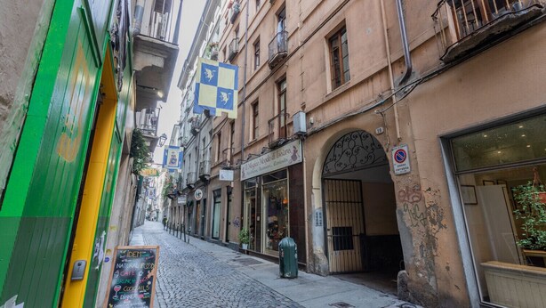 En brostensbelagt gade med en butik med grøn facade på venstre side og en bygning med skilt til restaurant på højre side.