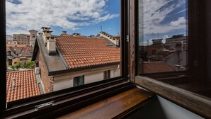 Udsigt fra et vindue over et bybillede med terracotta tagsten og en klar blå himmel.