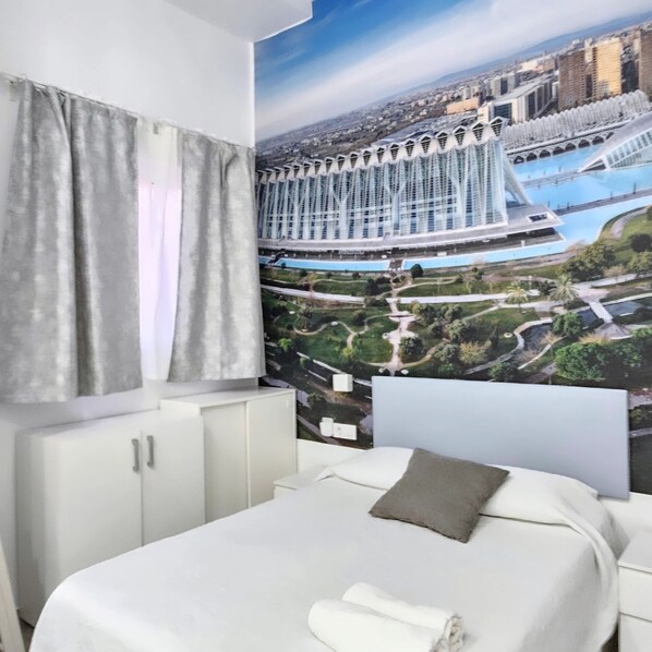 A bedroom with a bed, a window with curtains, a wall-mounted headboard, and a large cityscape mural.