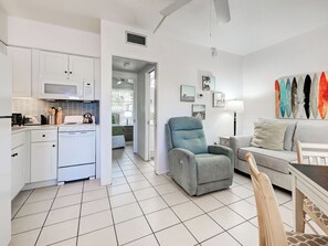 Un espace de vie compact comprenant un coin cuisine, un coin repas et un coin salon avec un canapé et un fauteuil.