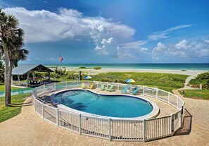 Una piscina con valla blanca, vista a la playa y una bandera.