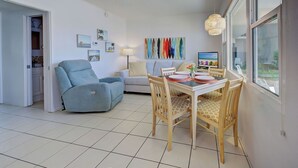 A modern living room with a dining area, a ceiling fan, a large window, and a colorful artwork on the wall. - Directly on the Gulf - Unit  4 - 1 Bedroom - Ground Floor - Sleeps up to 6] (Venice)
