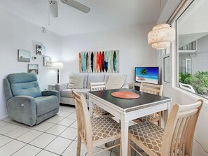 A modern living room with a sofa, a dining table with chairs, a TV, and artwork on the wall.