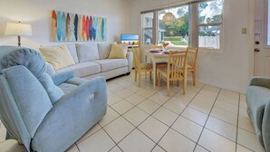 A living room with a sofa, a dining table with chairs, a TV, and a window with a view of the outdoors.