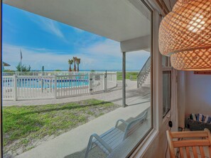 A balcony with a view of a swimming pool, a white fence, and a staircase leading to the pool area.