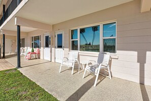A covered outdoor area with white chairs and a table, a small lawn, and a building with large windows and a view of palm trees. - Directly on the Gulf - Unit  4 - 1 Bedroom - Ground Floor - Sleeps up to 6] (Venice)