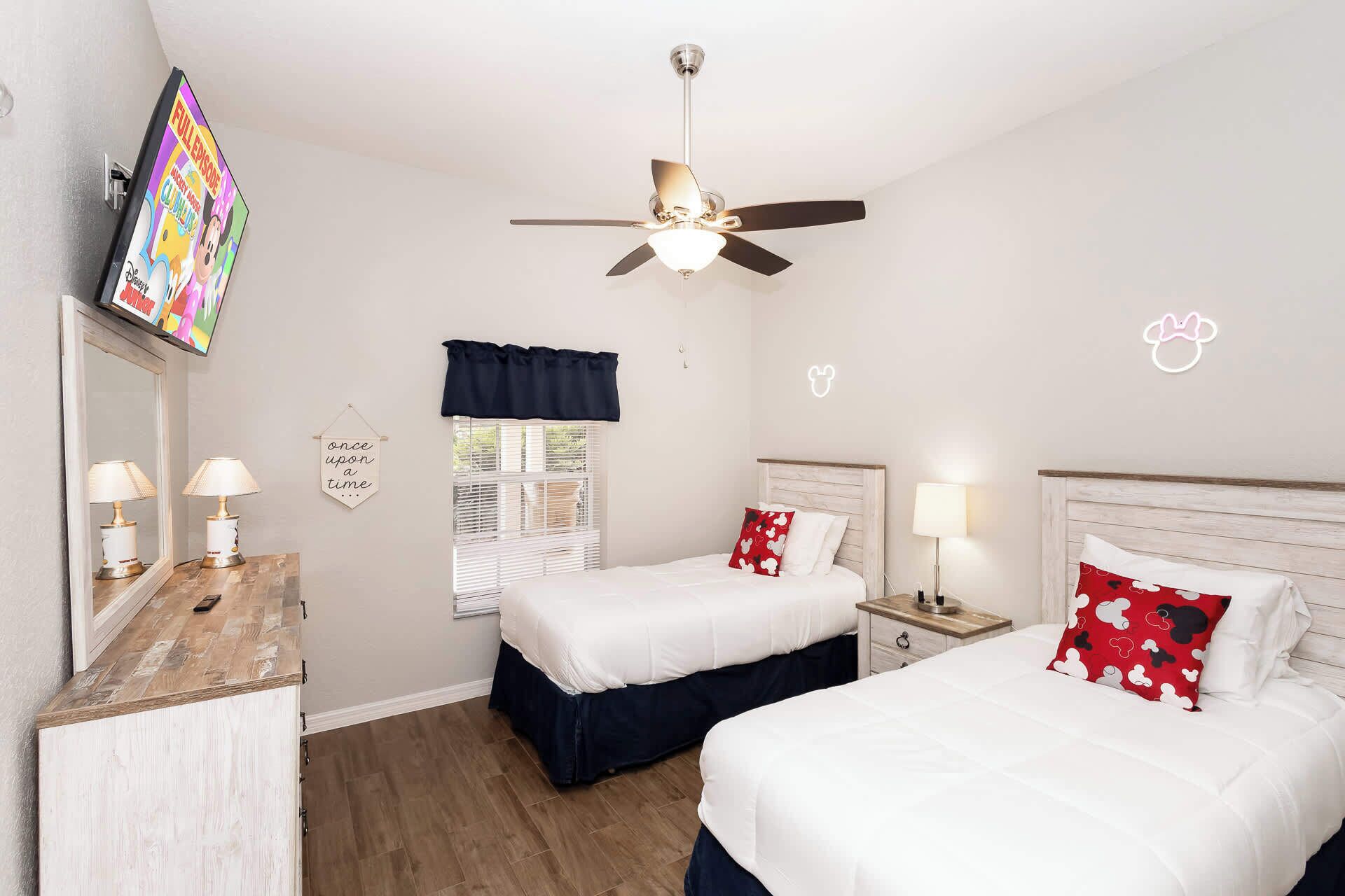 Habitación de hotel con dos camas, ventilador de techo, televisor y espejo.