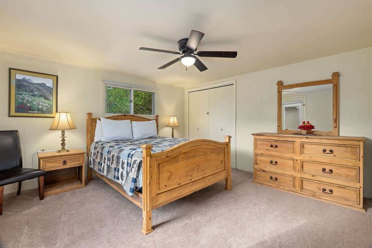 A bedroom with a wooden bed, bedside tables, a dresser, a ceiling fan, a window, and a mirror.