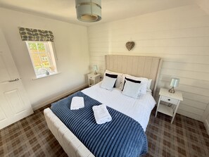A bedroom with a large bed, two bedside tables, a window with a view, and a heart-shaped decoration on the wall. - Stunning Coastal Cottage - Sleeping 6 in 3 Bedrooms - Pool and Beach Access Included. (Filey)